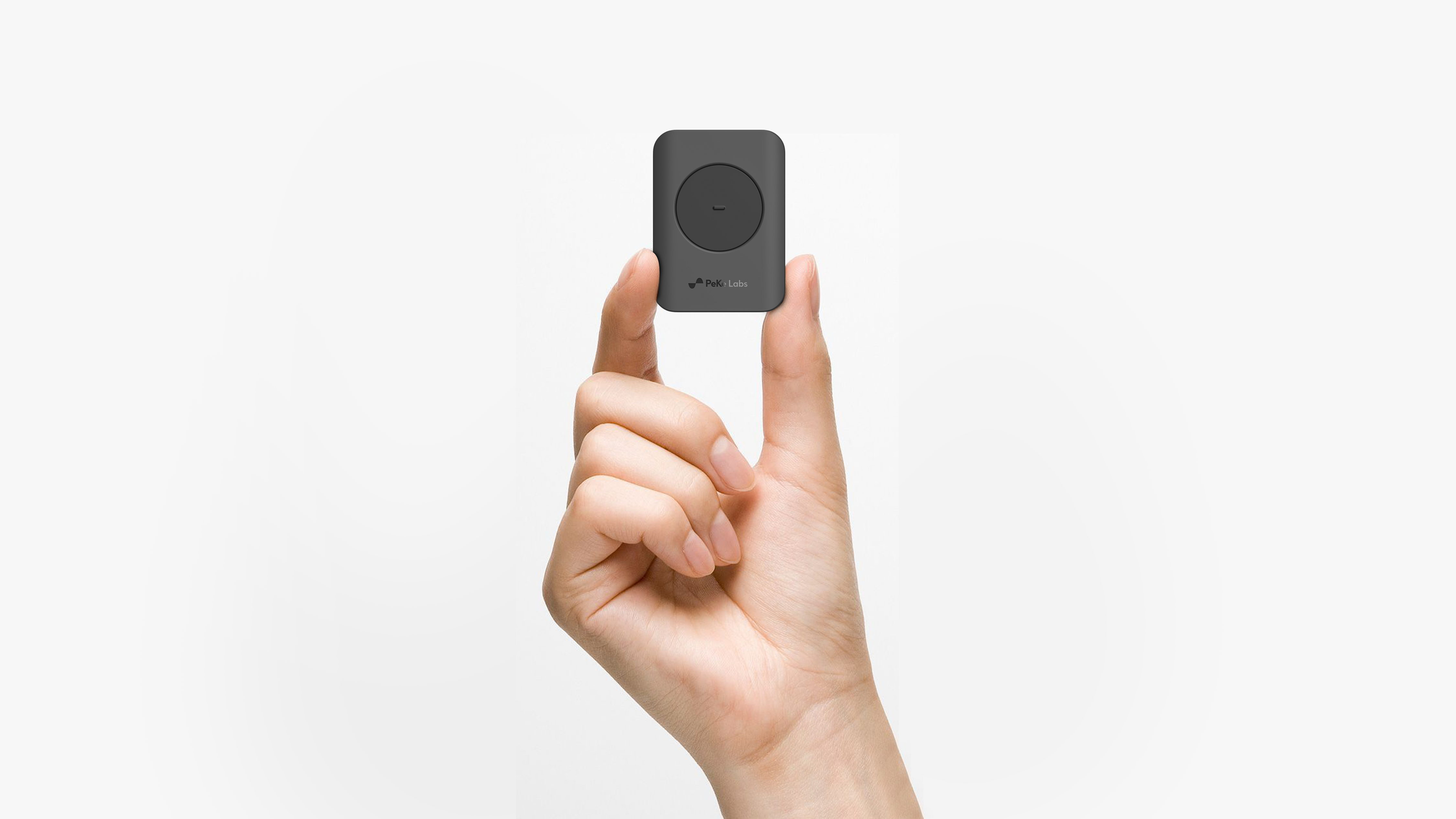 A hand holding the reference controller between two fingers - a small dark device with a circular touch pad.